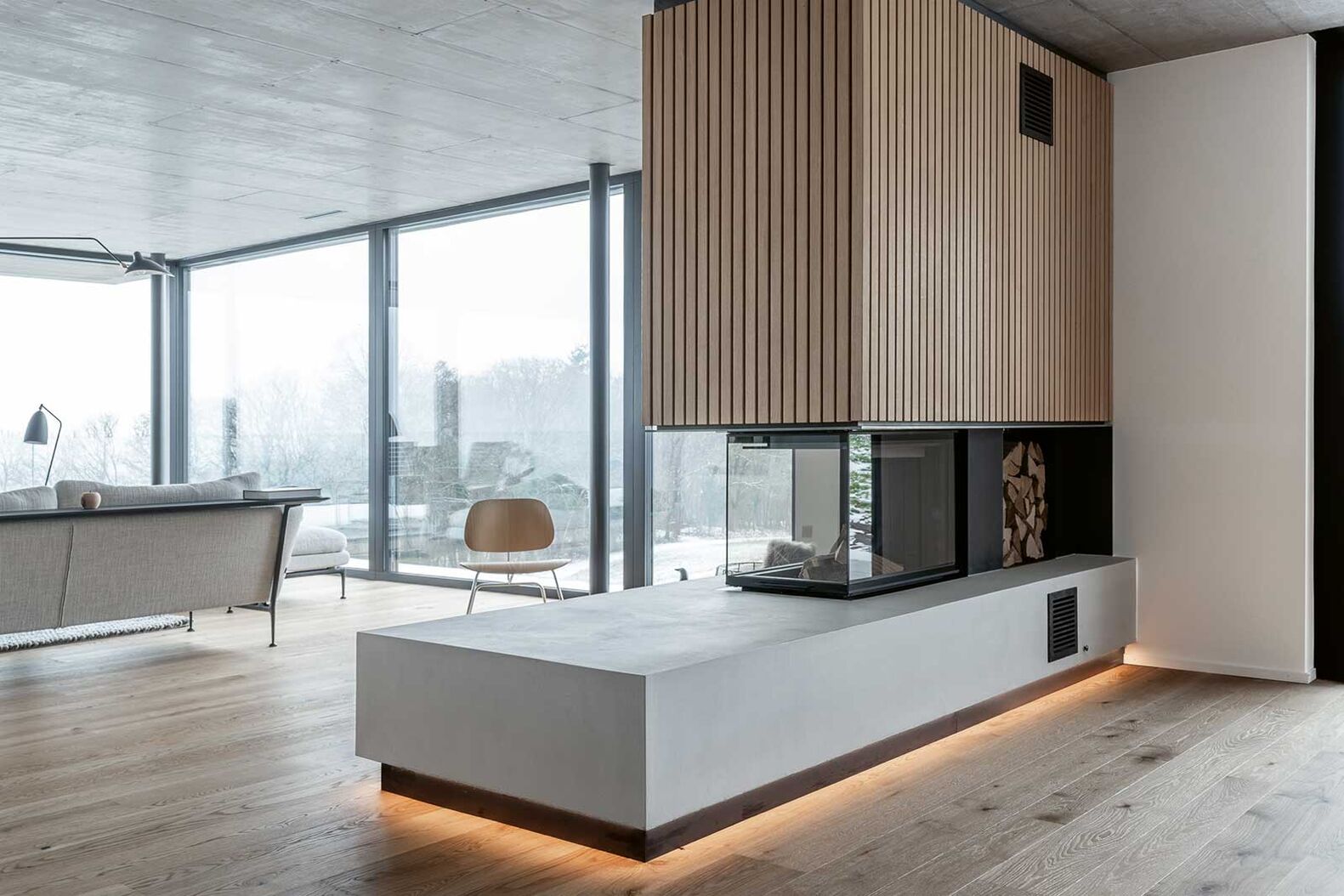 Atmosphärische Lichtspiele, selbst wenn der Kamin aus ist, sind hier zu sehen. Ein sanftes Ambiente durch indirekte Beleuchtung unten, ­Holztäfelung oben: So wird aus der Feuerstelle ein geschmackvoller Raumteiler. Glutform Müller GmbH, www.glutform.ch