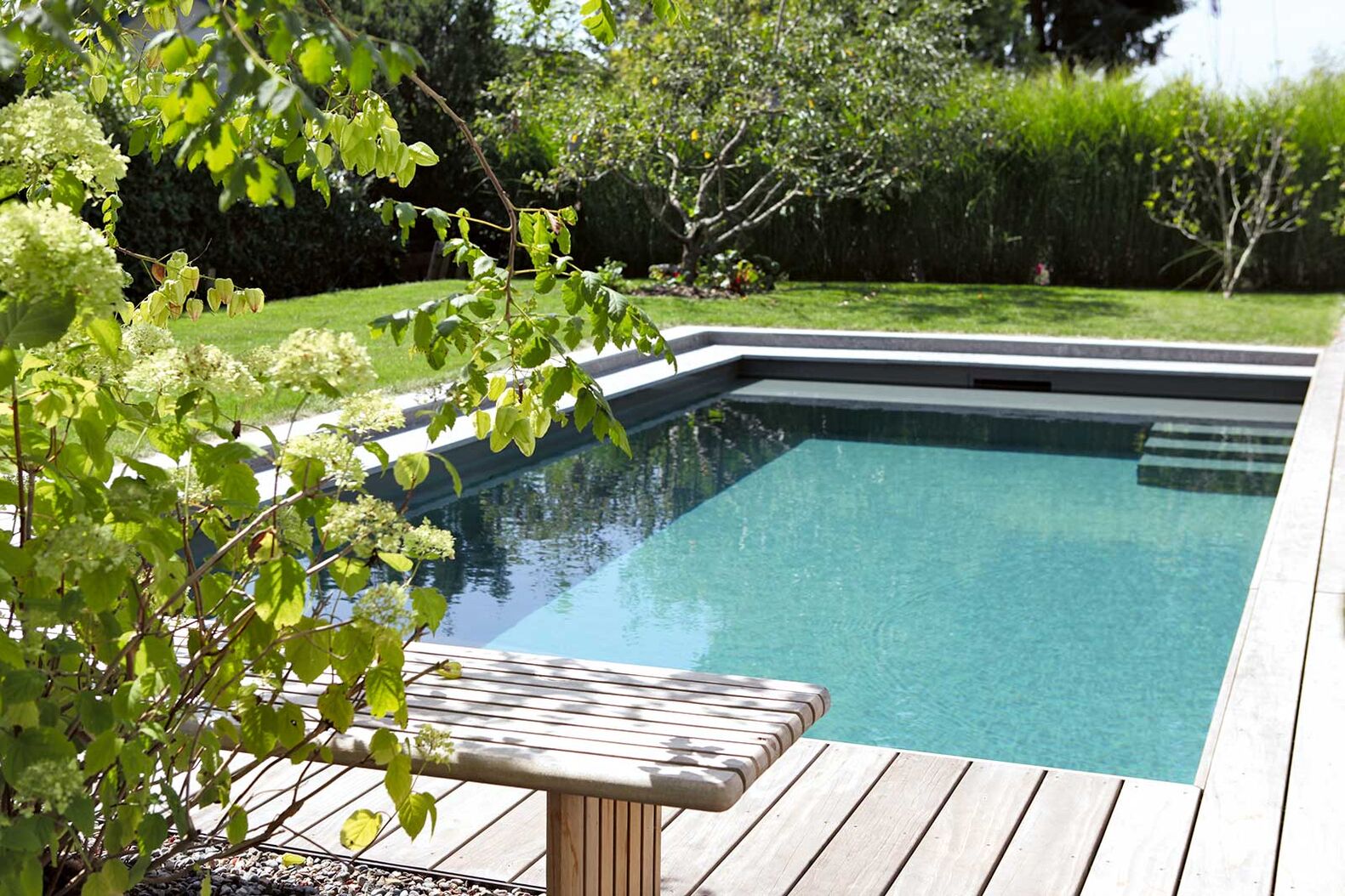 Biopool als Ruheinsel: Das Fertigbecken mit dem umlaufenden Holzdeck kontrastiert mit den üppig grünen Blasenbäumen. Ein biologisches Filtersystem und eine Gegenstromanlage machen es zum Trainings- und Erlebnisort gleichermassen. Lehnert AG, www.gartenzentrum.ch