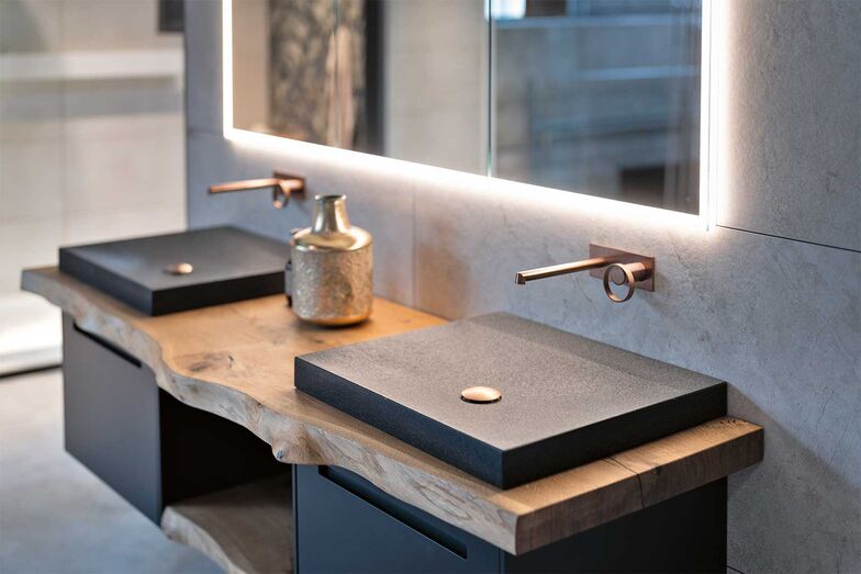 Becken aus Granit haben eine angenehme Haptik. Die Kombination aus Stein, massivem Holz und kupferfarbenen Armaturen bringt eine zeitlose Eleganz in jedes Bad.
