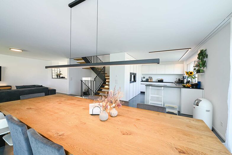 Moderne Küchentechnik mit Dunstabzug im Kochfeld schaffen eine lichte, einladende Atmosphäre zwischen Küche und Essplatz.