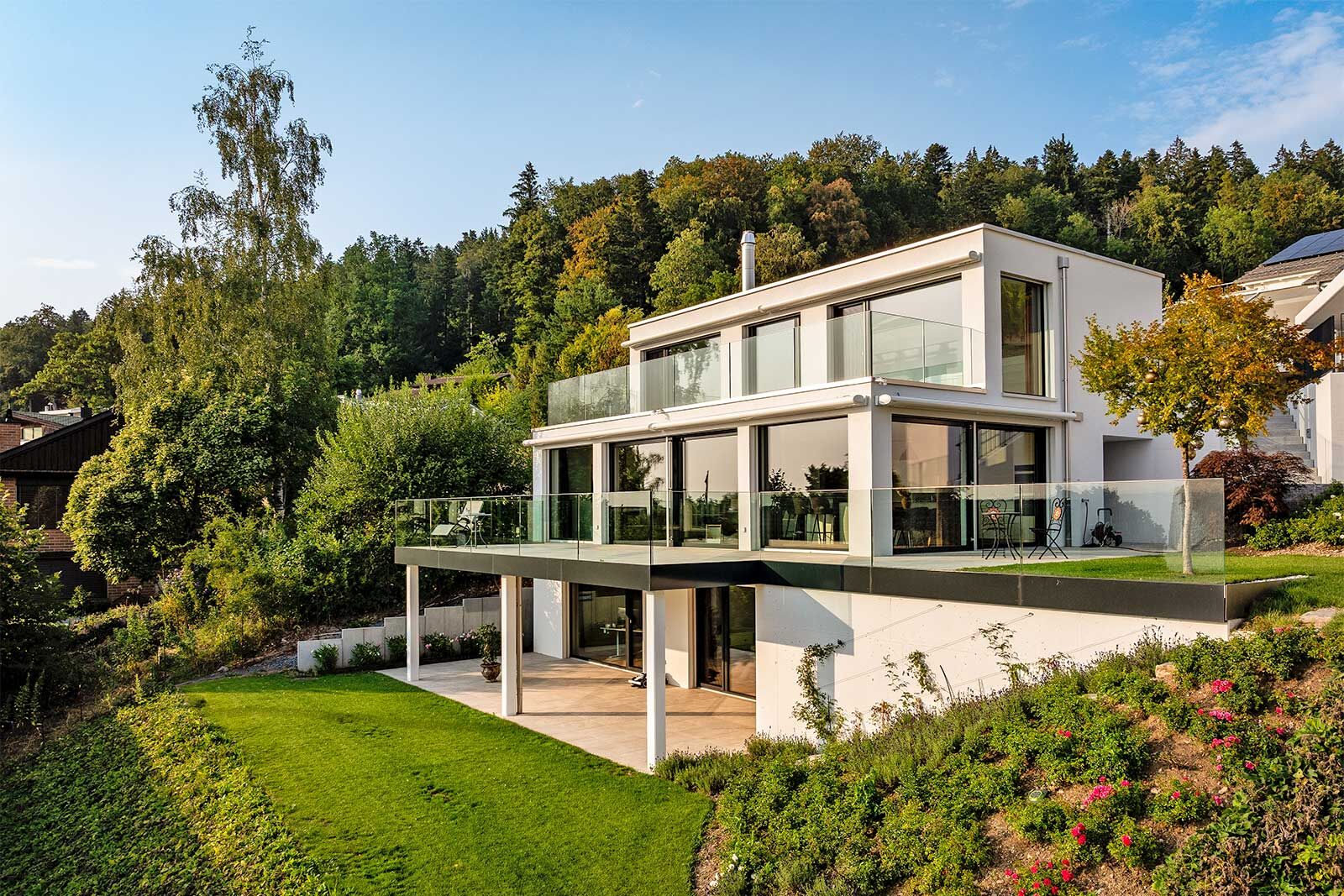 Terrassiert in den Hang gebaut, öffnet sich das moderne Einfamilienhaus mit raumhohen Fensterfronten zur Landschaft.