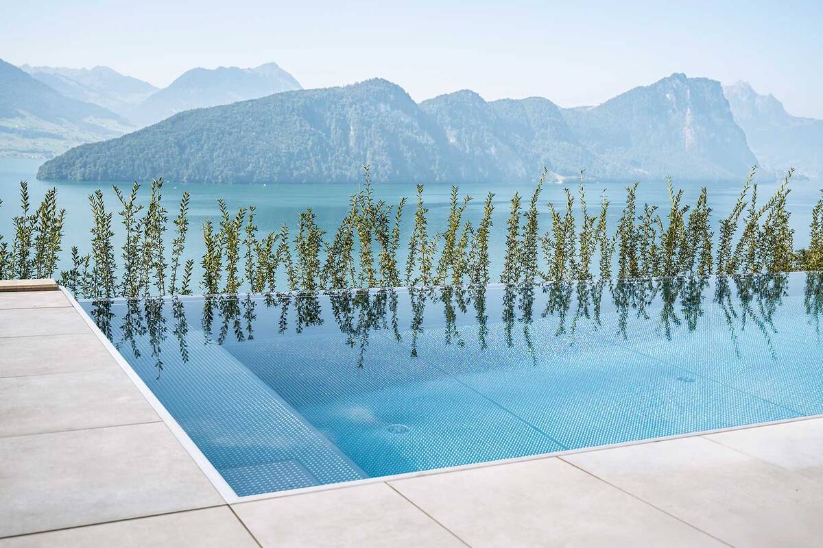 Der Edelstahl-Infinity-Pool mit den Massen 8 × 3,6 × 1,35 Meter fügt sich harmonisch in die Hanglage ein. Die Infinity-Rinne verschmilzt optisch nahtlos mit dem See und der Berglandschaft, während die schwebende Edelstahltreppe einen besonders leichten und modernen Einstieg ermöglicht. Mit hochwertiger Technik, effizienter Beheizung und einer Photovoltaikanlage, die den gesamten Energiebedarf mitversorgt, entstand ein Pool, der höchsten Ansprüchen an Ästhetik, Komfort und Nachhaltigkeit gerecht wird. Zireg.
