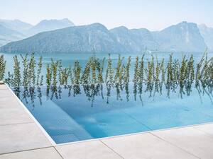 Der Edelstahl-Infinity-Pool mit den Massen 8 × 3,6 × 1,35 Meter fügt sich harmonisch in die Hanglage ein. Die Infinity-Rinne verschmilzt optisch nahtlos mit dem See und der Berglandschaft, während die schwebende Edelstahltreppe einen besonders leichten und modernen Einstieg ermöglicht. Mit hochwertiger Technik, effizienter Beheizung und einer Photovoltaikanlage, die den gesamten Energiebedarf mitversorgt, entstand ein Pool, der höchsten Ansprüchen an Ästhetik, Komfort und Nachhaltigkeit gerecht wird. Zireg.