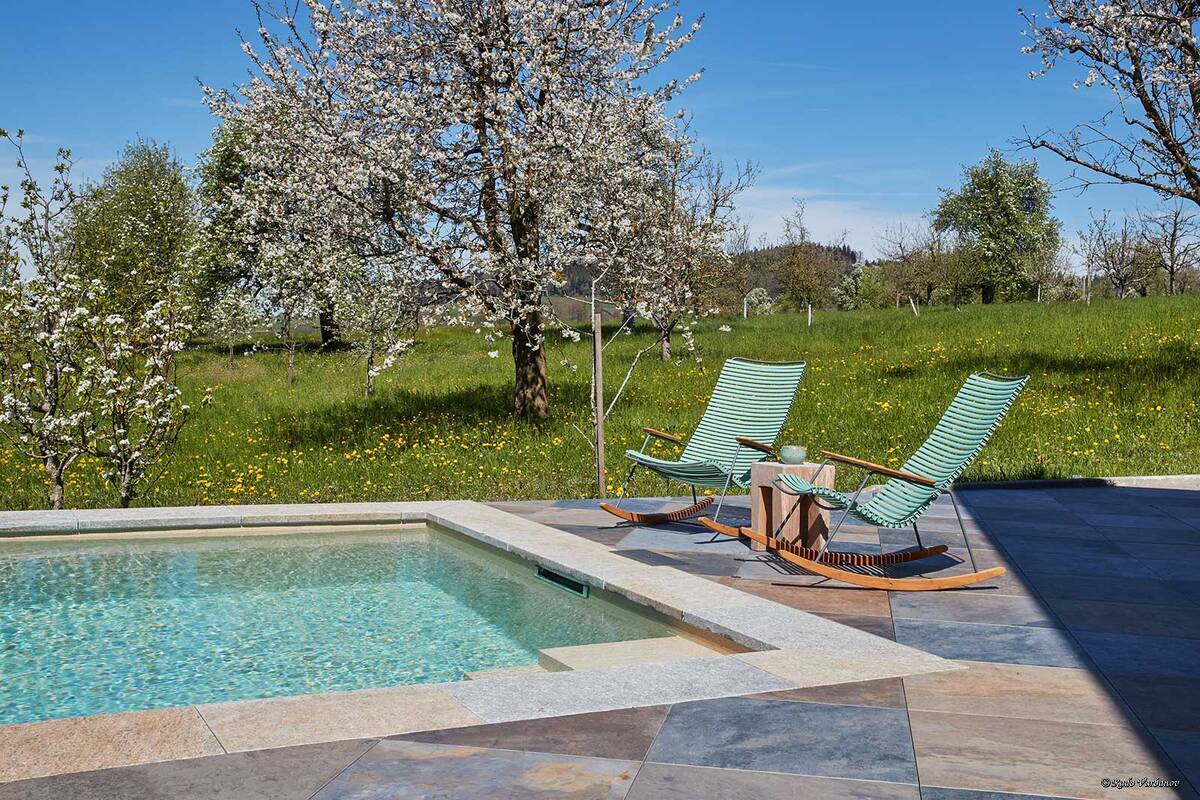 Das stilvolle Betonbecken, eingebettet in den Garten mit blühenden Obstbäumen, zeigt eindrucksvoll, dass ein Pool weit mehr sein kann als nur eine sommerliche Erfrischung. Der 10 × 3,30 × 1,50 Meter grosse Skimmer-Pool überzeugt mit hochwertiger Ausstattung: Die edle Folie Alkorplan Touch Relax, sechs Düsen und drei Unterwasserlampen sorgen für Komfort und stimmungsvolles Licht. Für optimale Wasserqualität sorgt eine moderne Salzaufbereitung. Vitabad.