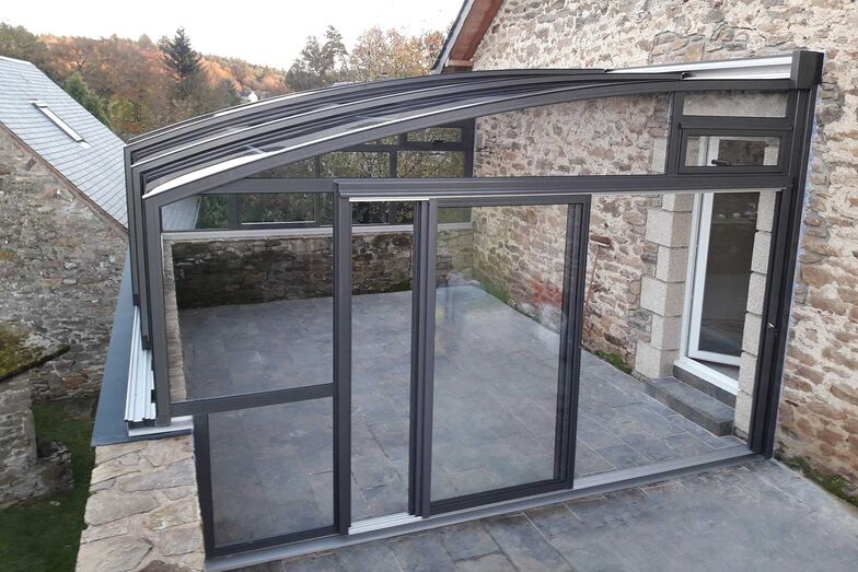 Bei dieser Terrassenüberdachung «Topas Solar Veranda» ist das Schiebesystem auf einer Steinmauer montiert, während die gegenüberliegende Seite entlang der Hauswand verläuft. So wird die Terrassenfläche optimal genutzt. Die Elemente lassen sich zur Seite schieben, sodass wahlweise eine geschlossene Überdachung oder ein luftiges Terrassengefühl entsteht. Die bodengleiche Ausführung der Stirnwand ermöglicht einen direkten Zugang.