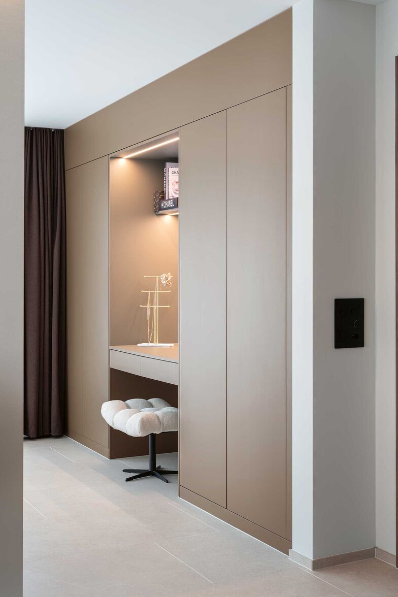 Dieser Einbauschrank besticht durch eine beleuchtete Schminknische. Er ist Teil eines eleganten graubraunen Schranksystems von Elbau, das von der Garderobe bis zum Bad vielfältige Staumöglichkeiten schafft. Elbau Küchen AG, www.elbau.ch